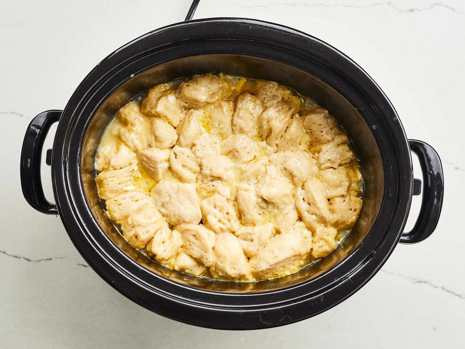 A bowl of creamy chicken and dumplings with tender chicken pieces, carrots, and fluffy dumplings, set on a wooden table with a spoon and linen napkin