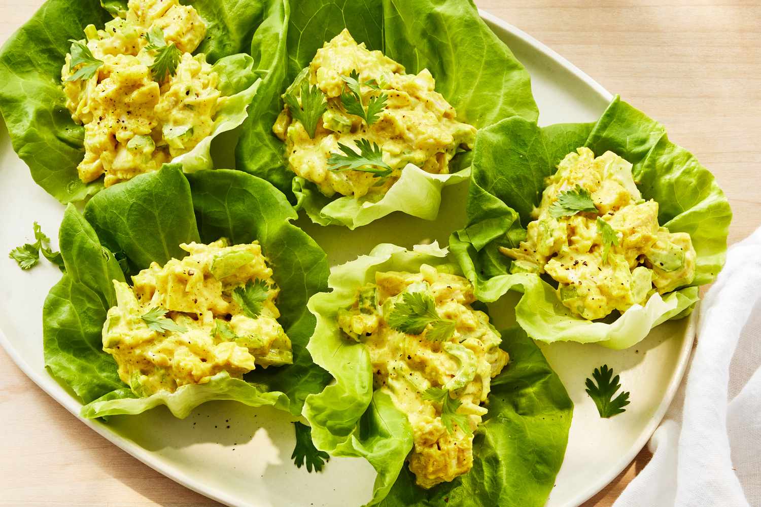 A bowl of creamy curry chicken salad with grapes, celery, and toasted almonds on a sunlit kitchen table, with a toasted croissant and lettuce nearby