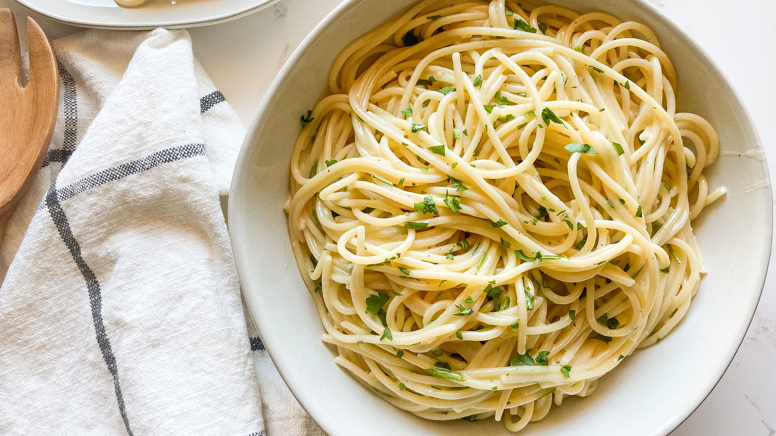 A bowl of creamy garlic butter pasta topped with black pepper and grated Parmesan on a wooden table with a fork beside it, warm kitchen lighting