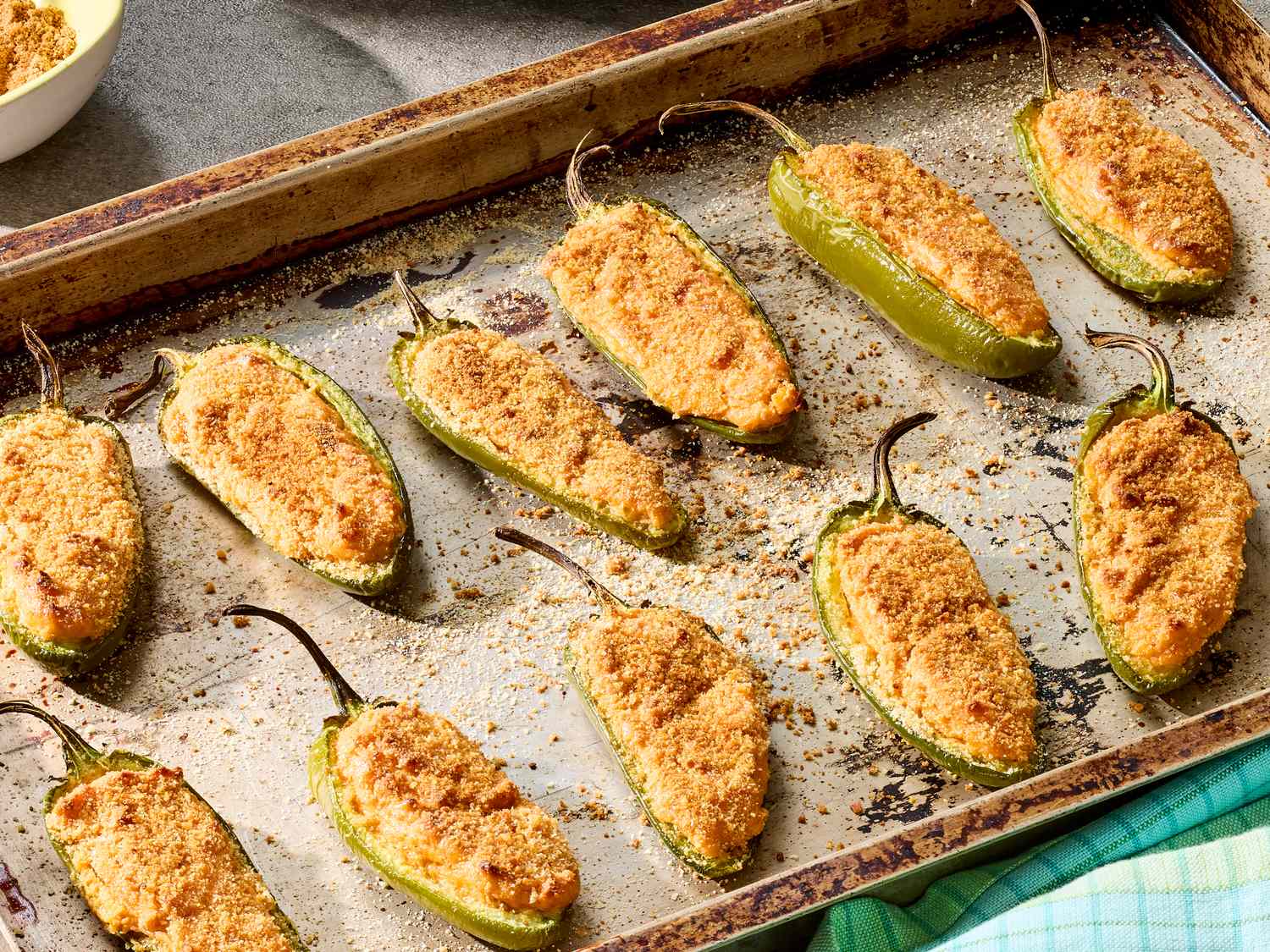 A bowl of creamy jalapeño filling with visible green jalapeño bits and shredded cheddar on a light kitchen counter, with a spoon resting in the mixture