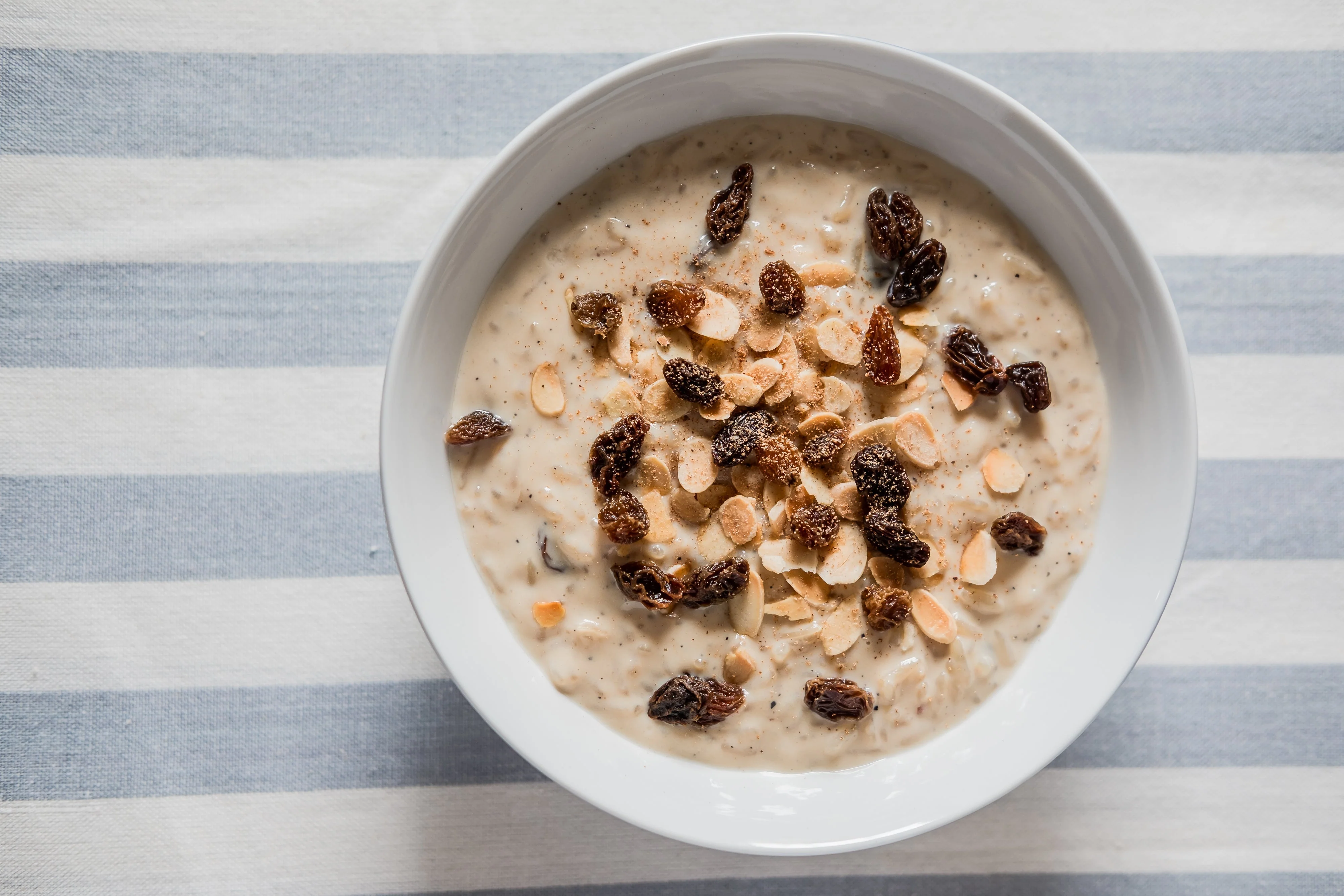 A bowl of creamy kheer rice pudding garnished with sliced almonds and pistachios on a warm-toned kitchen table with a spoon beside it