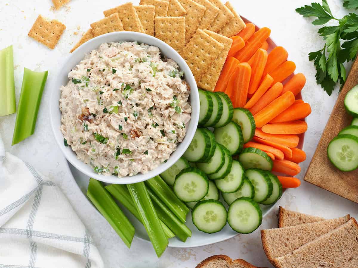 A bowl of creamy tuna salad with chopped celery and herbs beside toasted bread on a kitchen counter