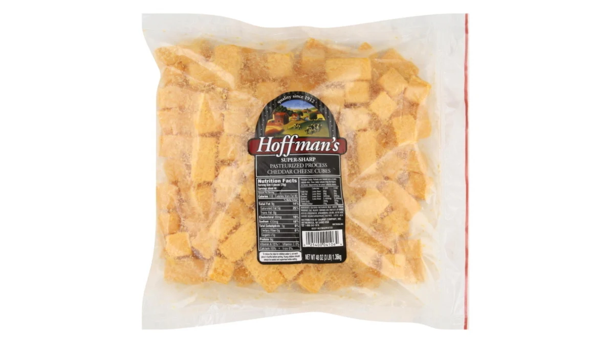 A bowl of cubed processed cheese on a kitchen counter next to a measuring cup of milk