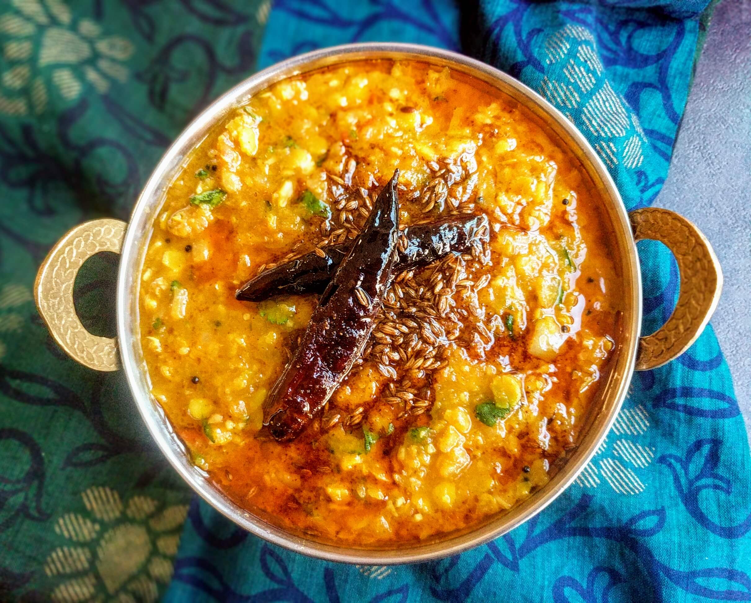 A bowl of dal tadka topped with sizzling cumin-garlic tadka, chopped cilantro, and a wedge of lemon on a simple wooden table