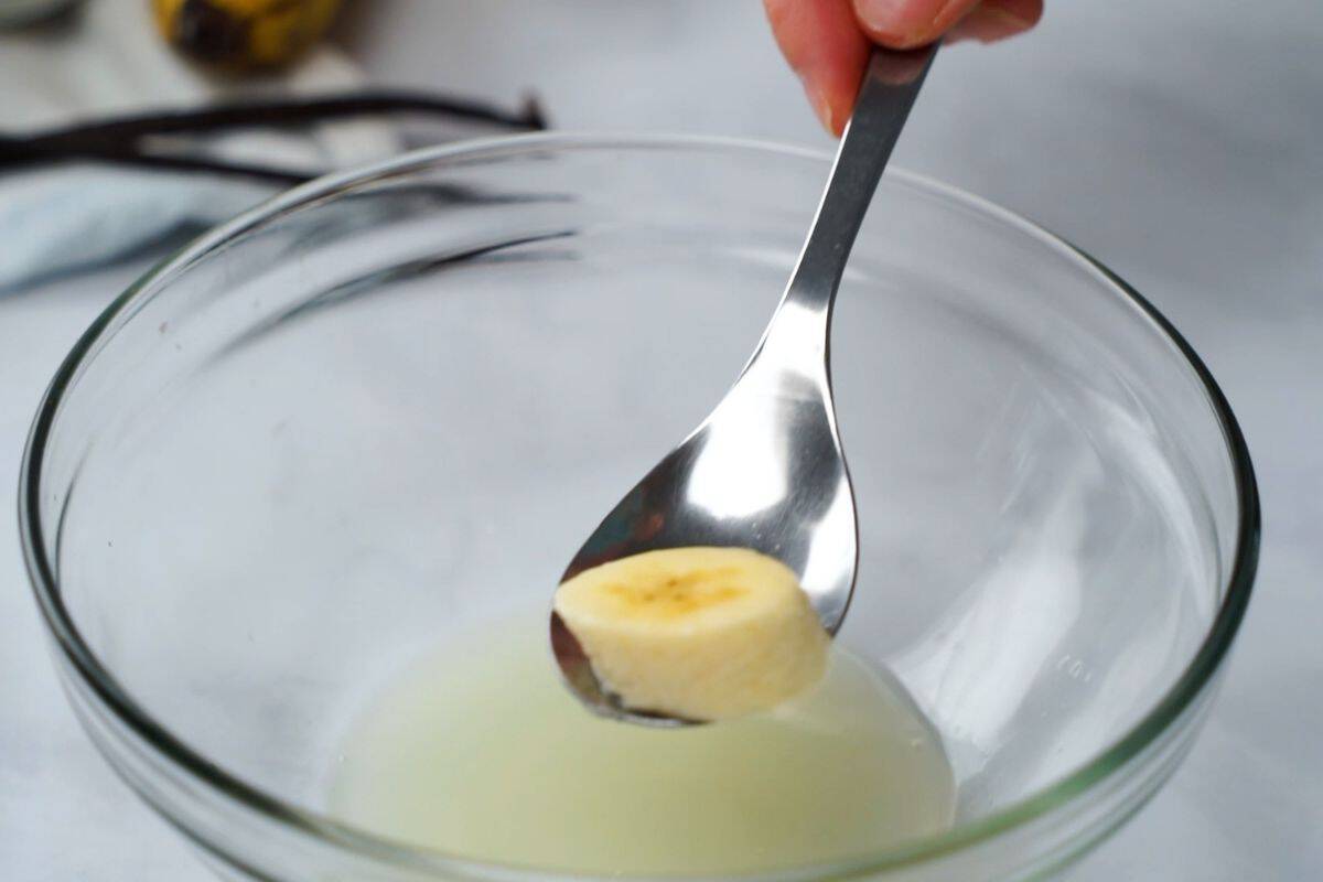 A bowl of freshly sliced bananas being gently tossed with a small squeeze of lemon juice on a kitchen counter