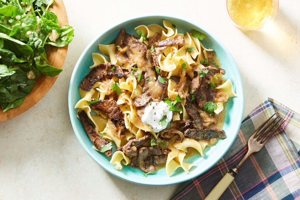 A bowl of garlic butter steak pasta with sliced medium-rare steak, glossy Parmesan sauce, and chopped parsley on a neutral linen napkin