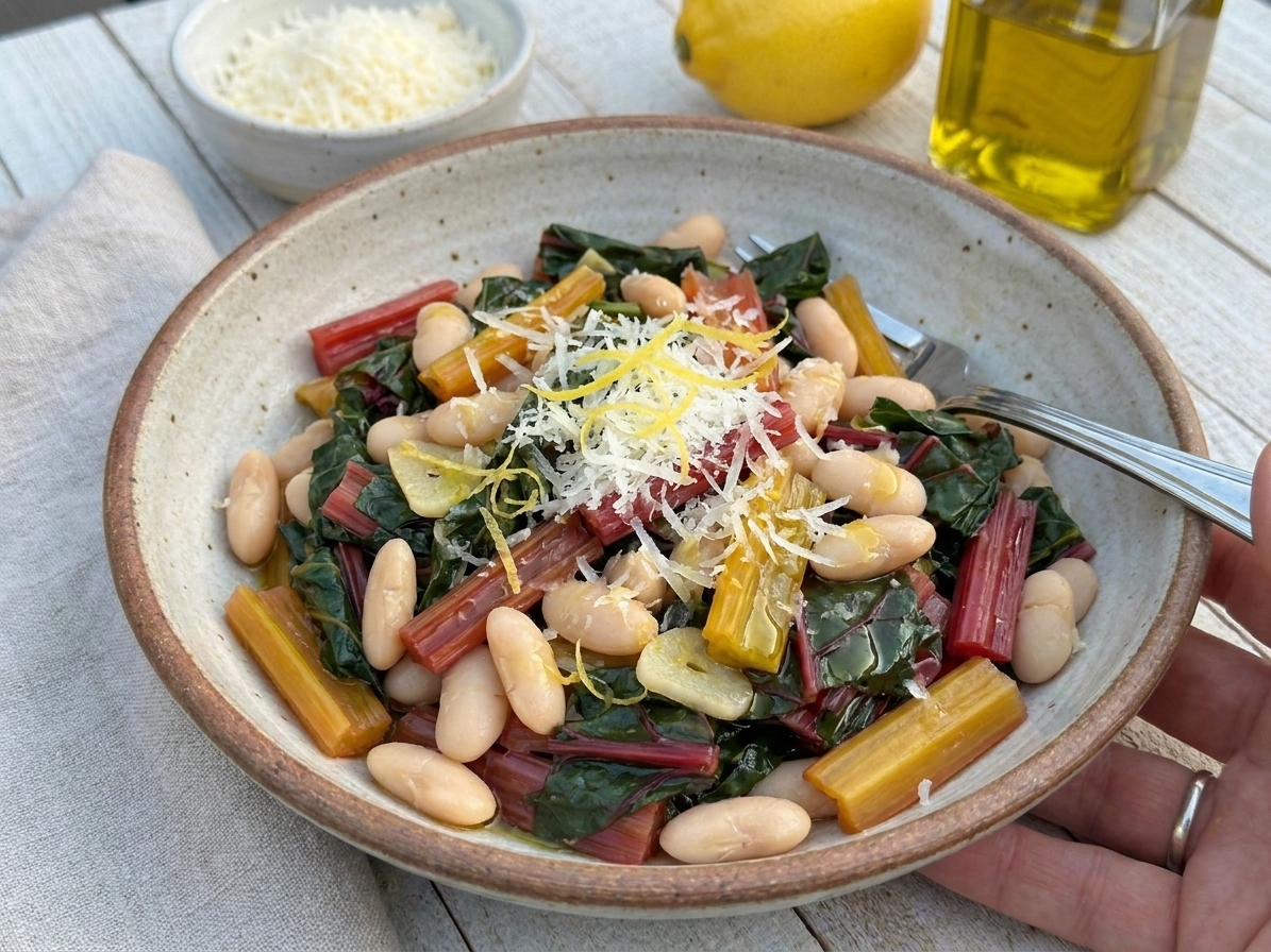 A bowl of garlicky Swiss chard and white beans topped with grated Parmesan, lemon zest, and a drizzle of olive oil