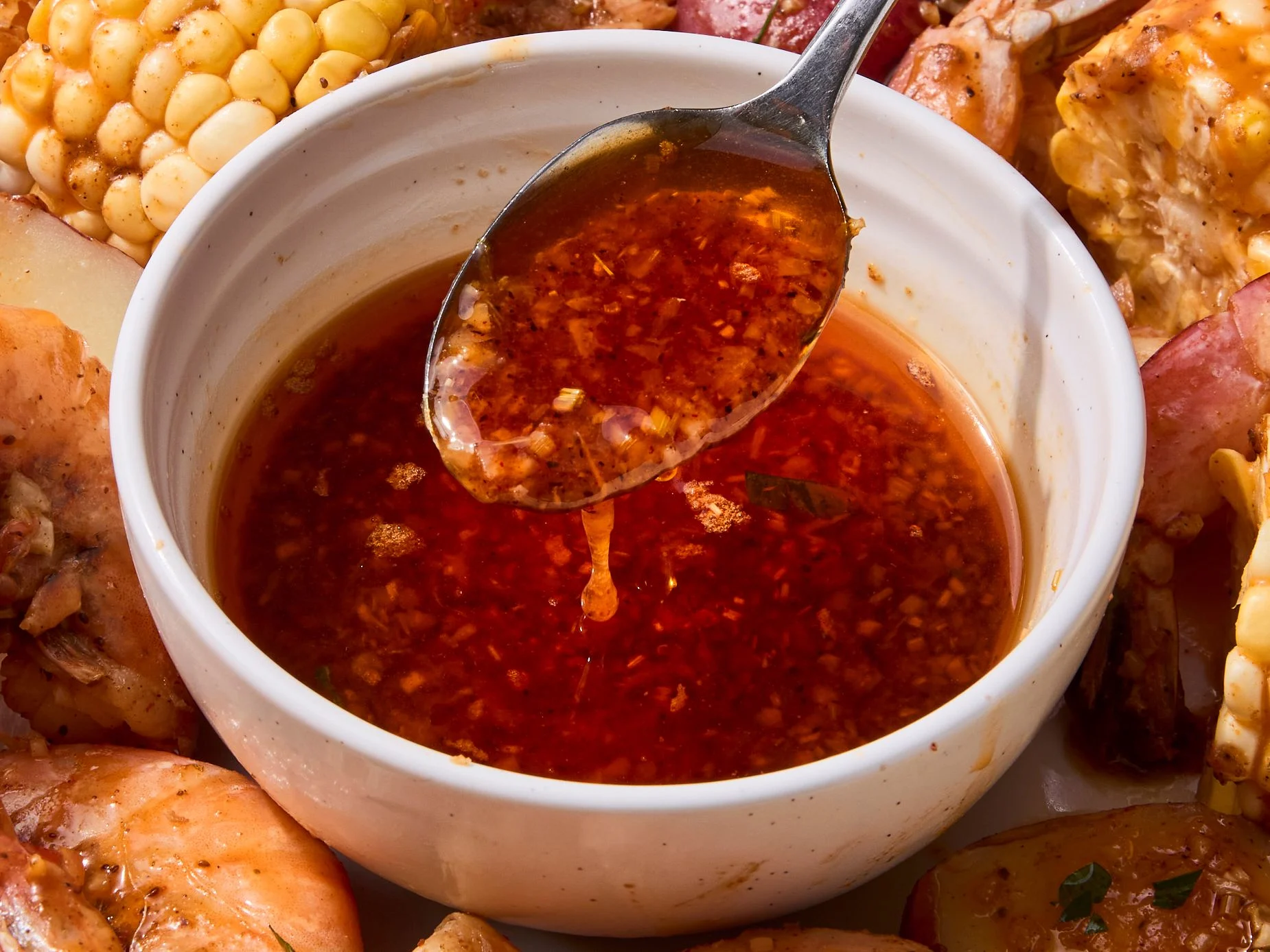 A bowl of glossy seafood boil sauce with visible minced garlic and paprika, set on a warm kitchen counter beside lemon wedges and a spoon