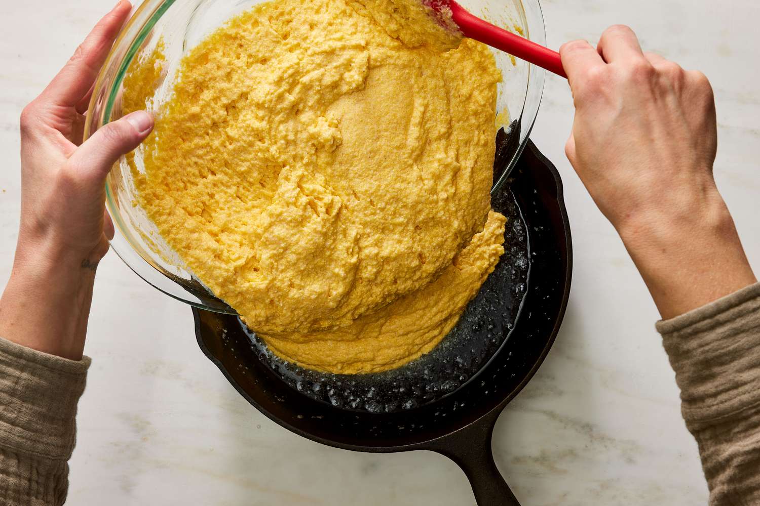 A bowl of gluten free cornbread batter being whisked on a kitchen counter, with cornmeal visible and a whisk resting in the bowl