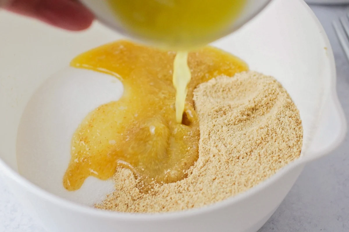 A bowl of graham cracker crumbs being mixed with melted butter using a fork on a kitchen counter