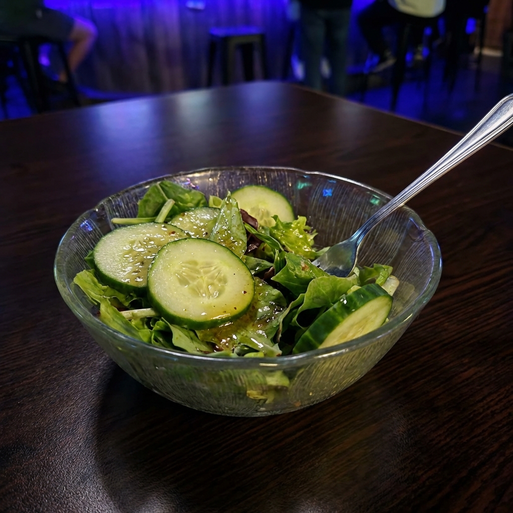 A bowl of green salad with cucumbers and vinaigrette