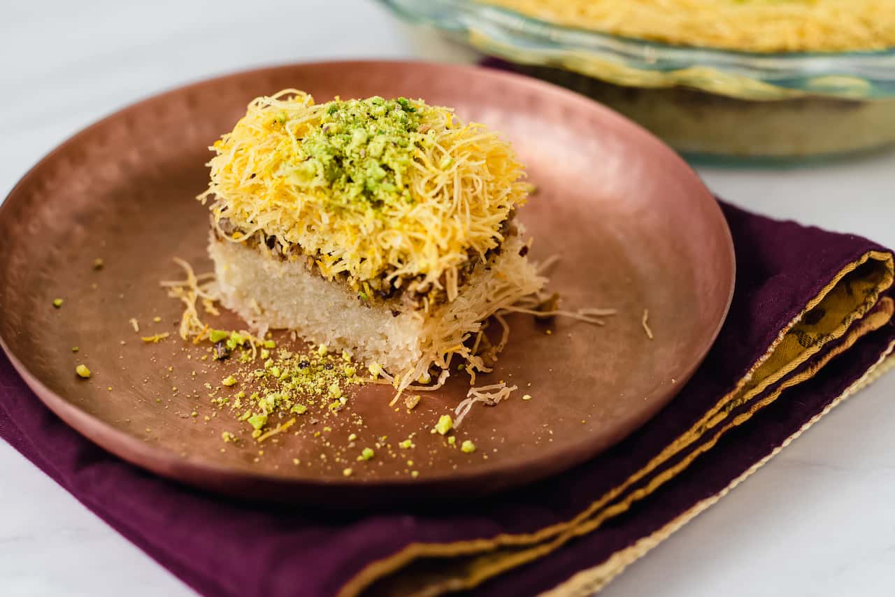 A bowl of kataifi shredded phyllo pastry on a kitchen counter beside melted butter and a mixing spoon
