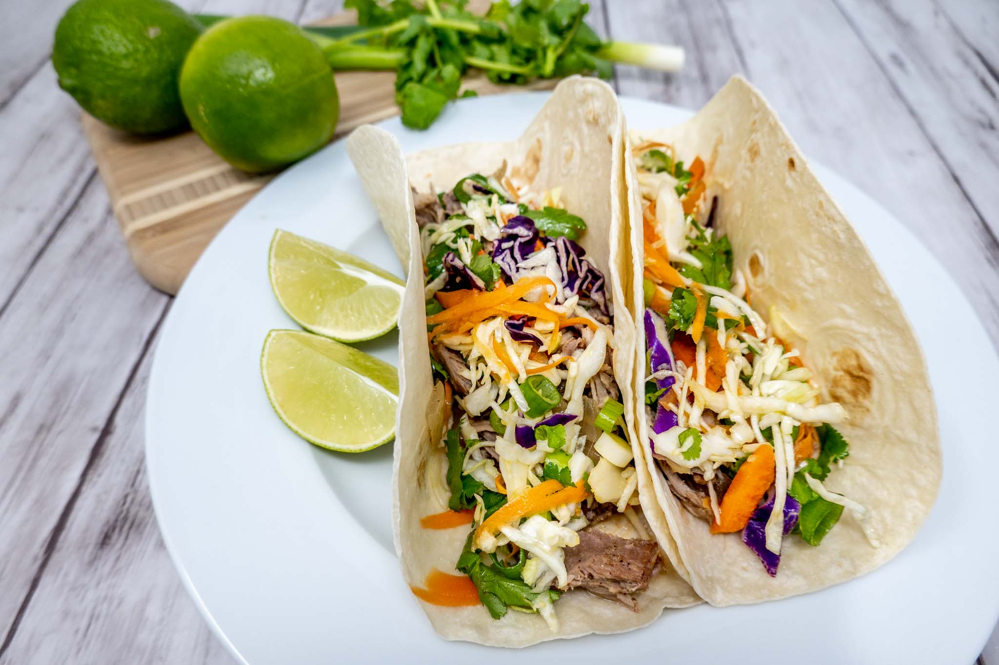 A bowl of leftover barbecue pulled pork next to tortillas, cabbage, lime, and a small bowl of mayonnaise on a clean kitchen counter in warm lighting