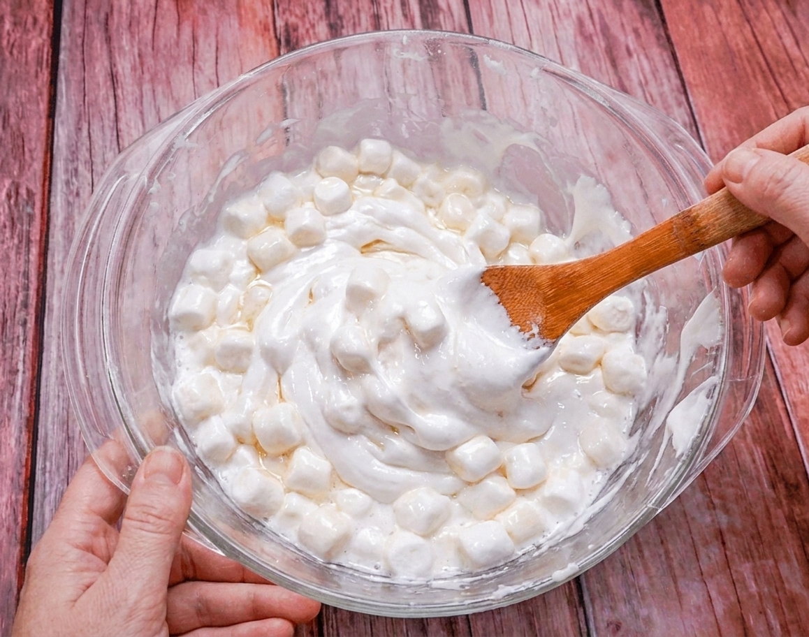 A bowl of marshmallows partially melted and glossy, being stirred midway through microwaving
