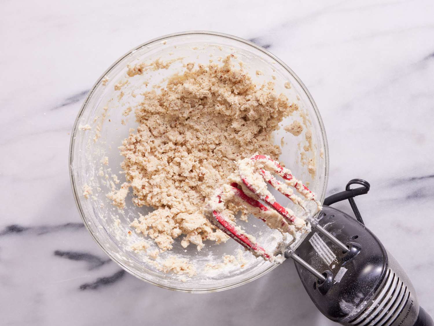 A bowl of pale cookie dough with chopped pecans mixed in, with a rubber spatula resting on the side