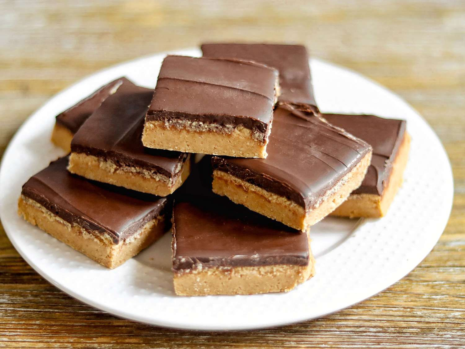 A bowl of peanut butter mixture being stirred with a rubber spatula on a kitchen counter, thick and glossy before pressing into a pan