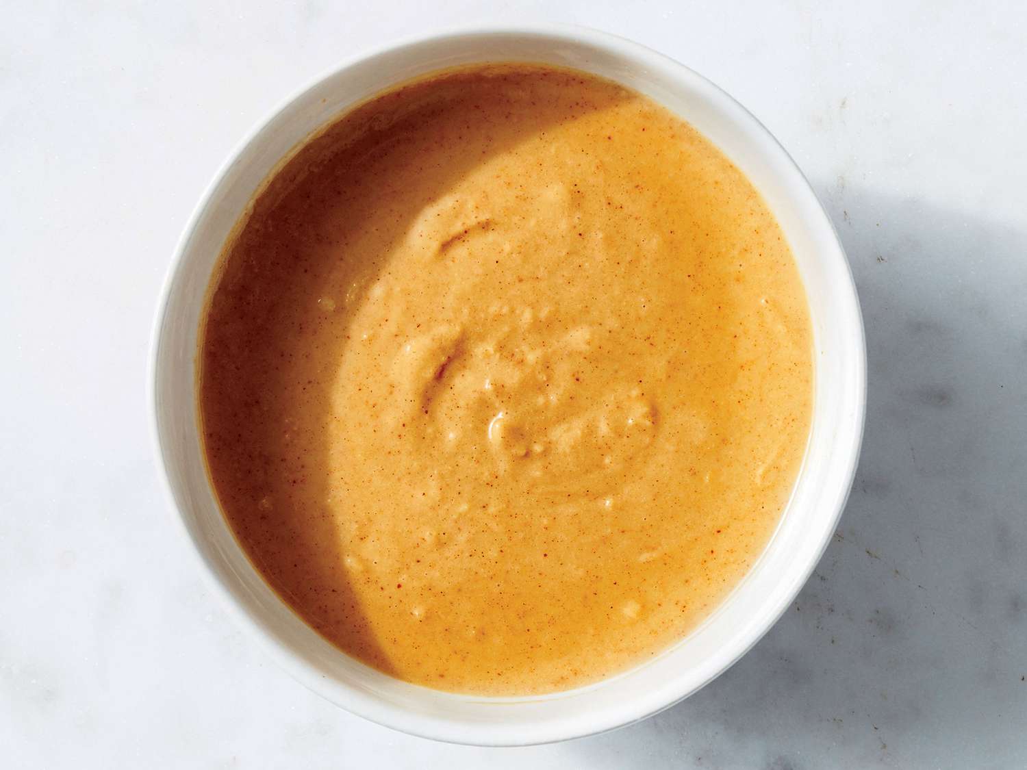A bowl of peanut sauce being whisked until smooth and glossy on a kitchen counter