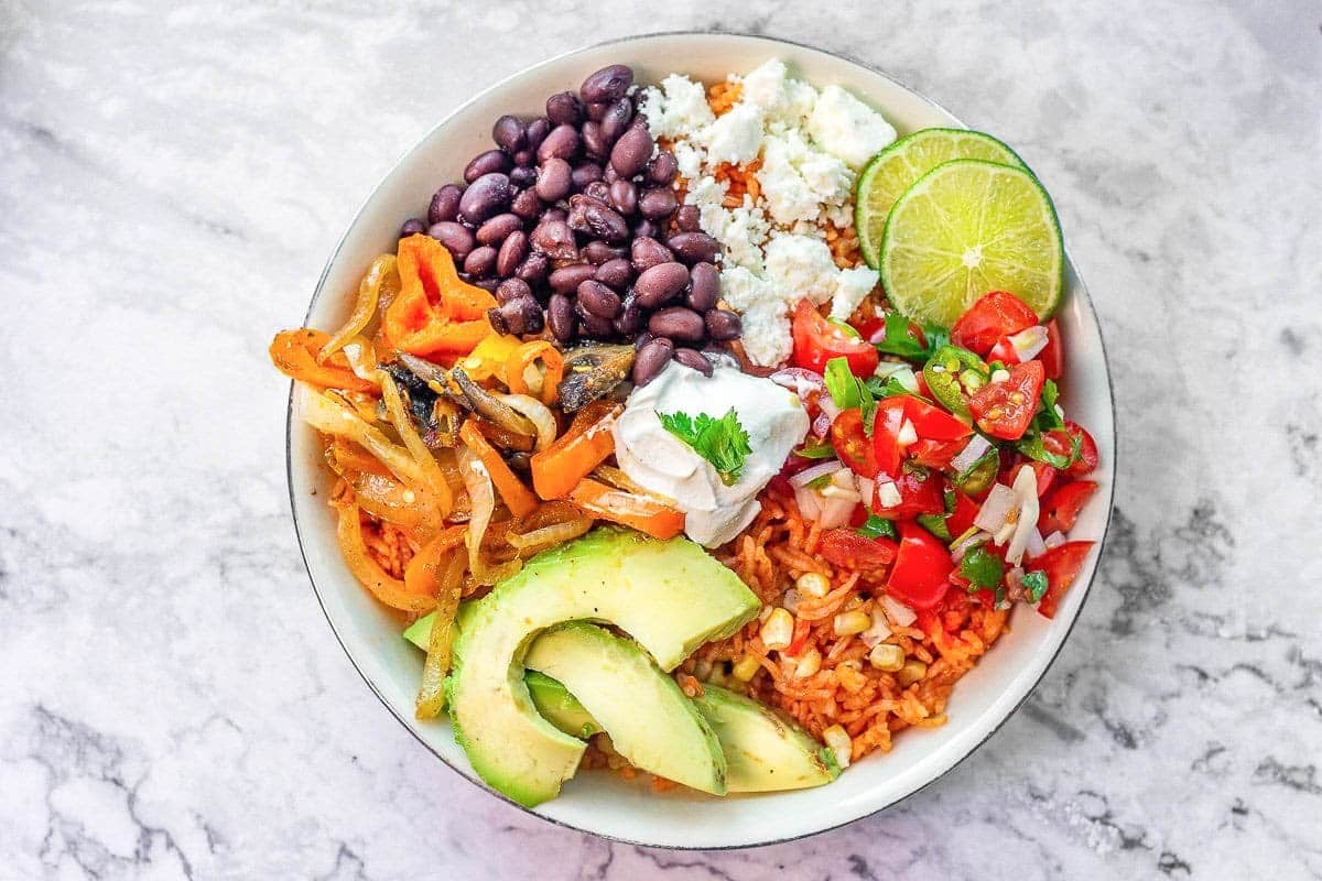 A bowl of saucy Mexican black beans topped with cilantro and crumbled queso beside fluffy rice on a wooden table in warm natural light