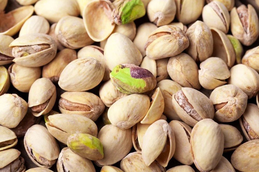 A bowl of shelled pistachios and a small pinch bowl of sea salt arranged on a clean kitchen counter with warm natural light