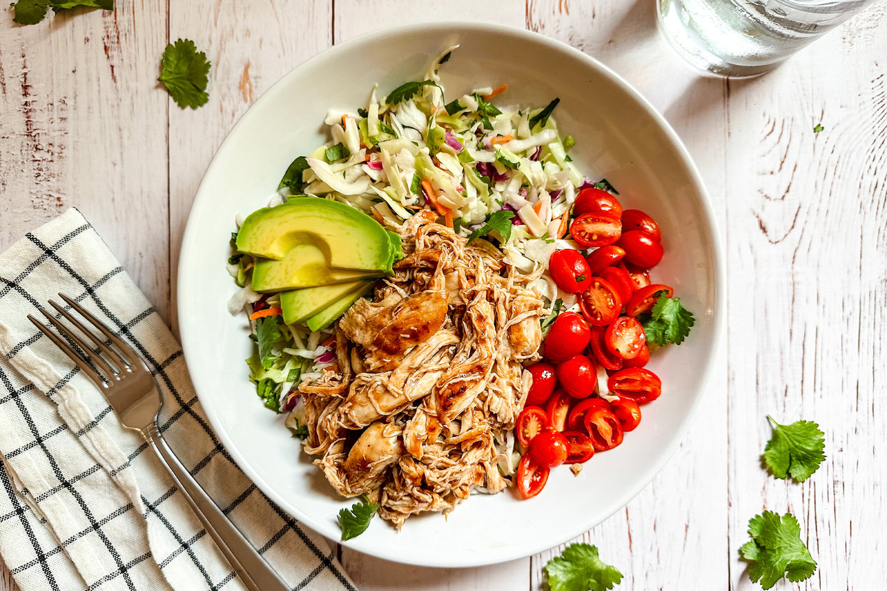 A bowl of shredded cooked chicken on a kitchen counter next to diced onion and celery, ready for casserole prep