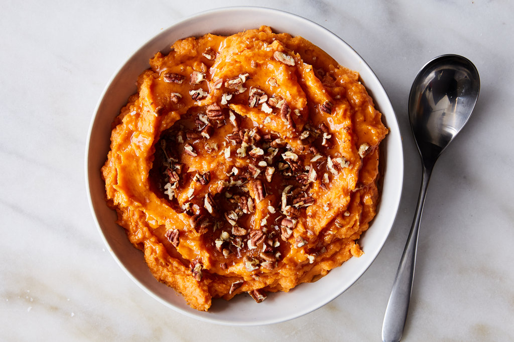 A bowl of smooth mashed sweet potato with a spoon resting in it on a kitchen counter
