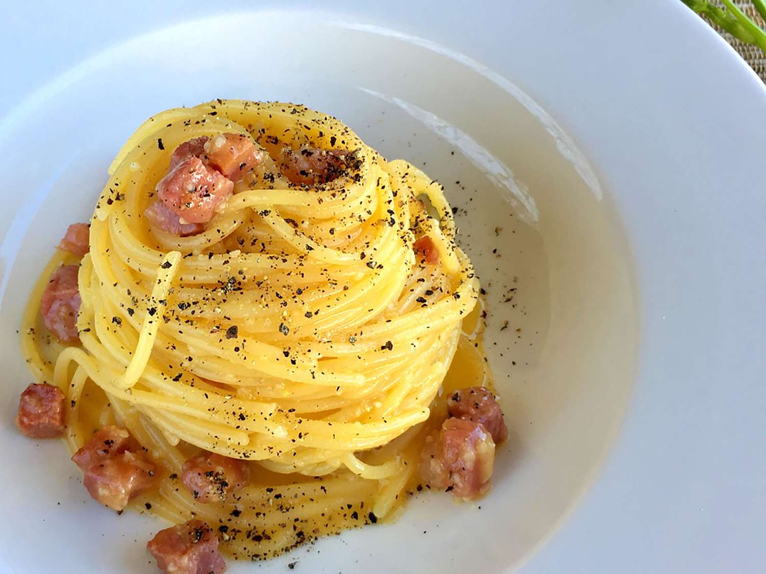 A bowl of spaghetti alla carbonara with glossy sauce, crisp guanciale pieces, and freshly cracked black pepper on top, set on a simple dinner table