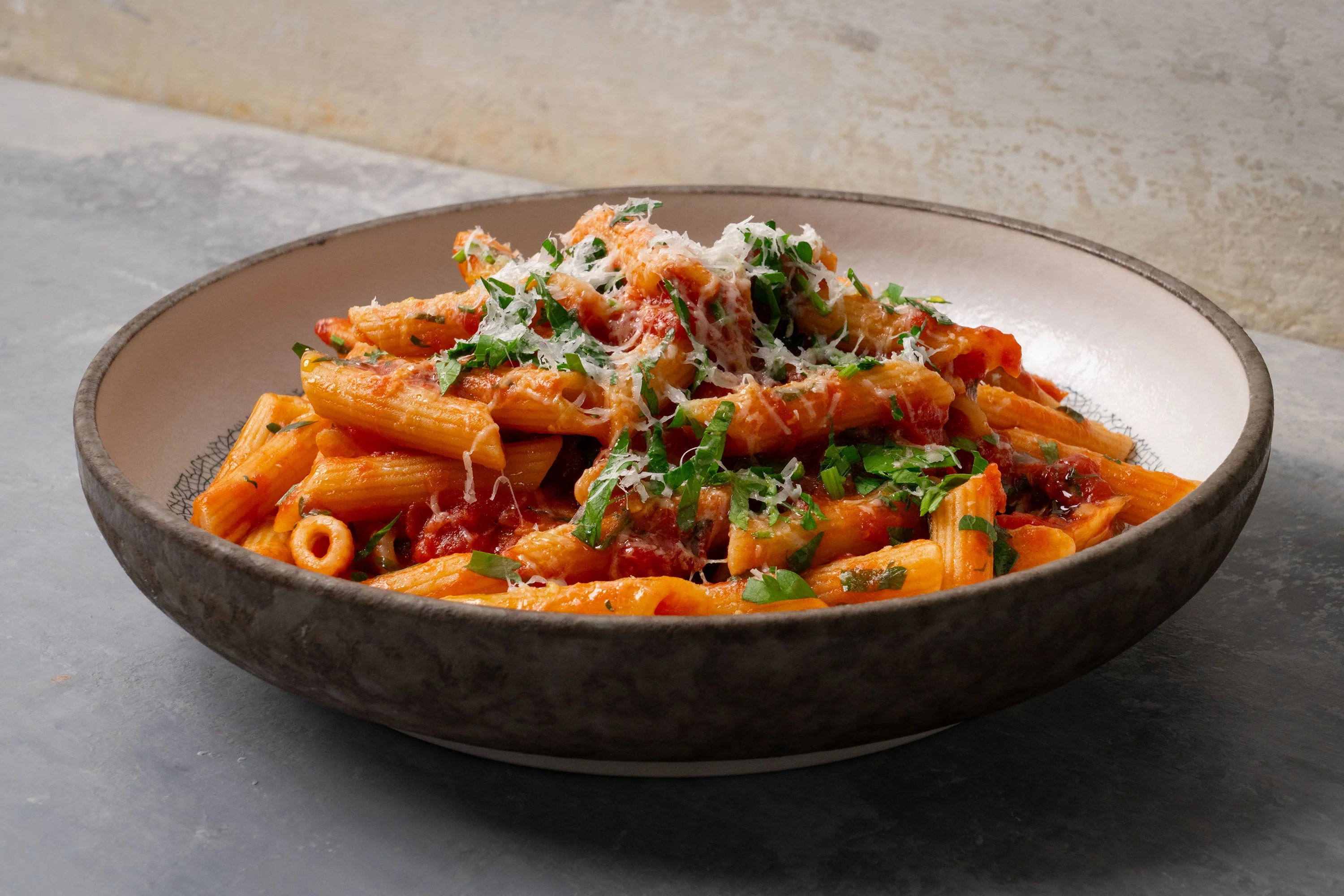 A bowl of spaghetti coated in glossy arrabbiata sauce with fresh basil on top, set on a warm-toned kitchen table with a fork and linen napkin