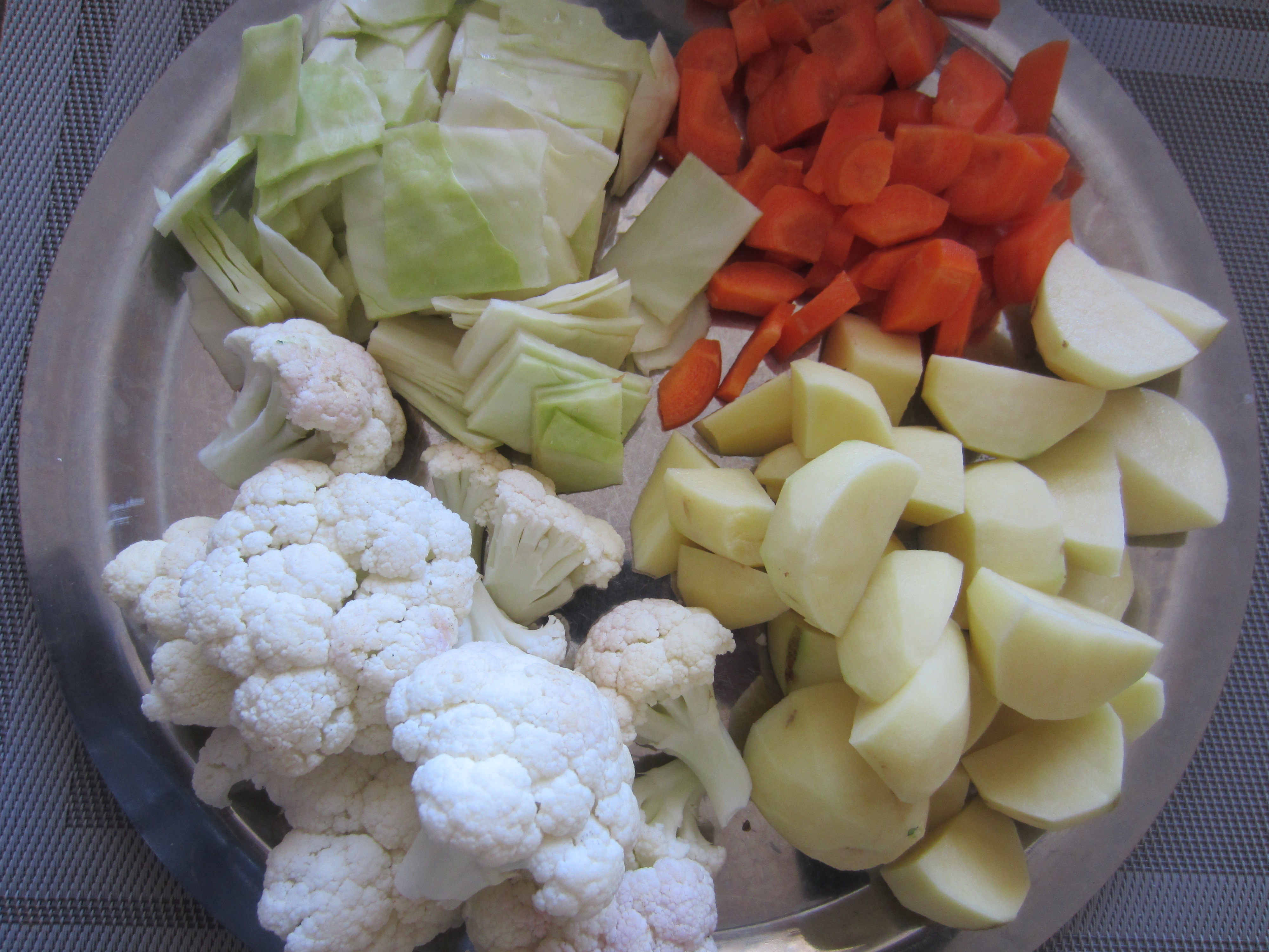 A bowl of tender boiled potatoes and cauliflower florets draining in a colander over a pot on a home stove