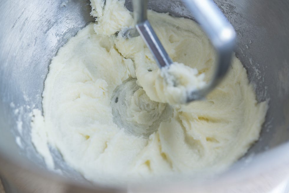 A bowl of thick vanilla cookie batter for black and white cookies with a spatula resting on the rim on a bright kitchen counter