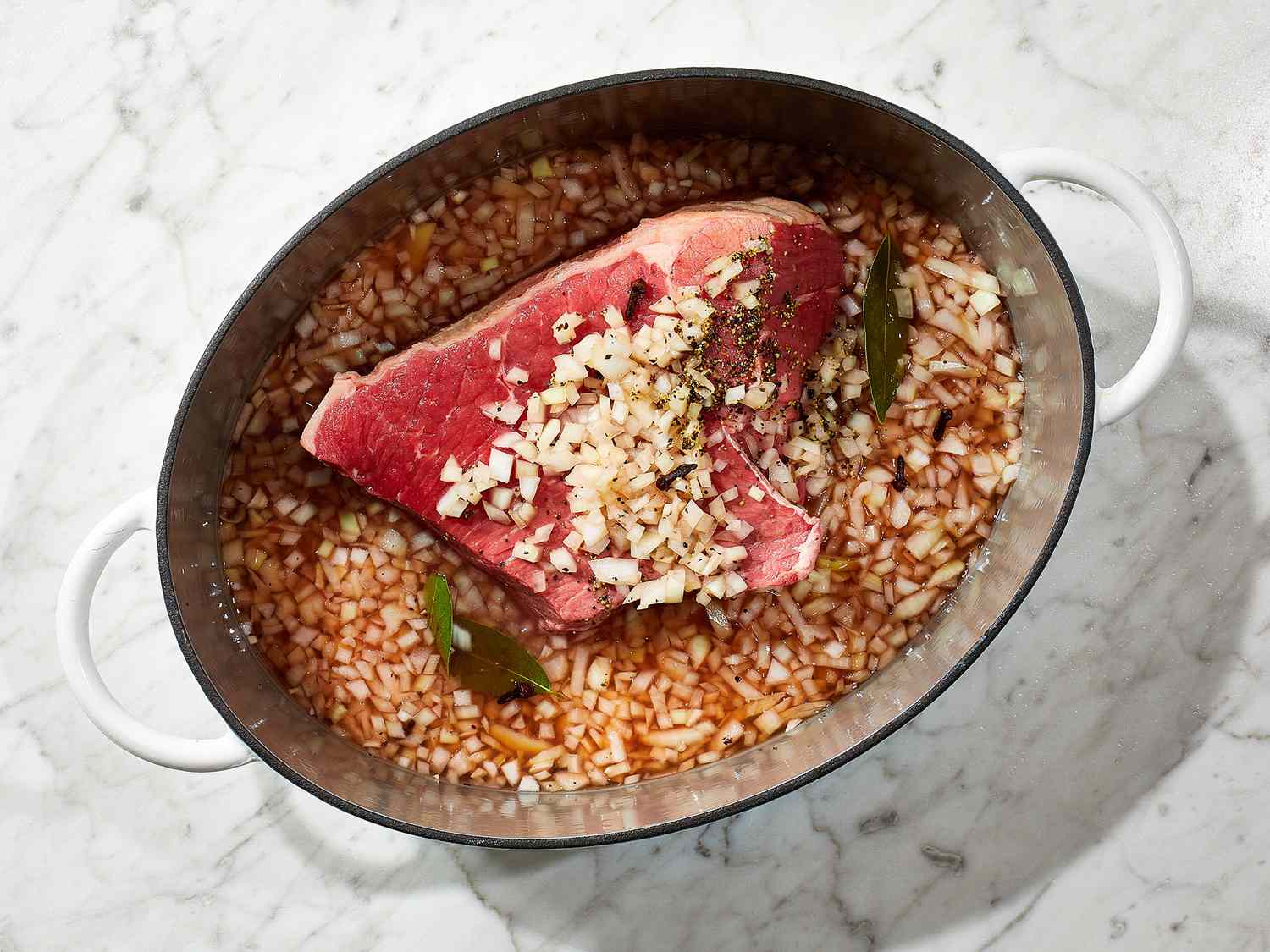 A bowl of vinegar-based sauerbraten marinade with sliced onions and whole spices, ready for a beef roast
