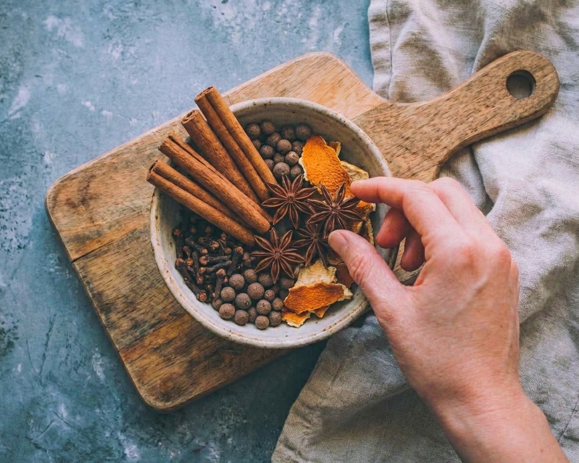 A bowl on a kitchen counter filled with whole cinnamon sticks, cloves, star anise, allspice berries, and orange peel ready for mulling