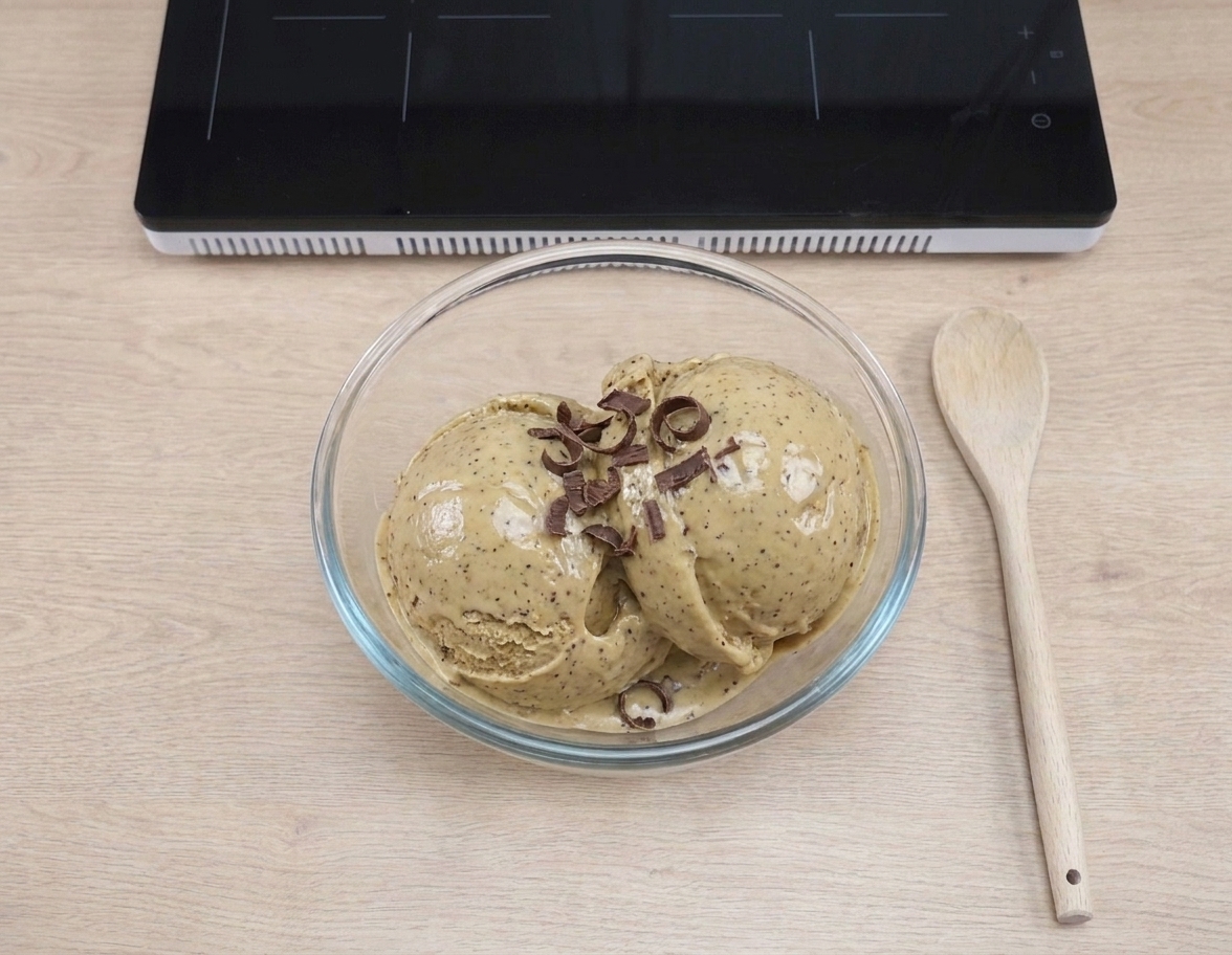 A bowl with two scoops of creamy coffee ice cream, glossy from fresh churning, topped with a few chocolate shavings on a neutral kitchen table