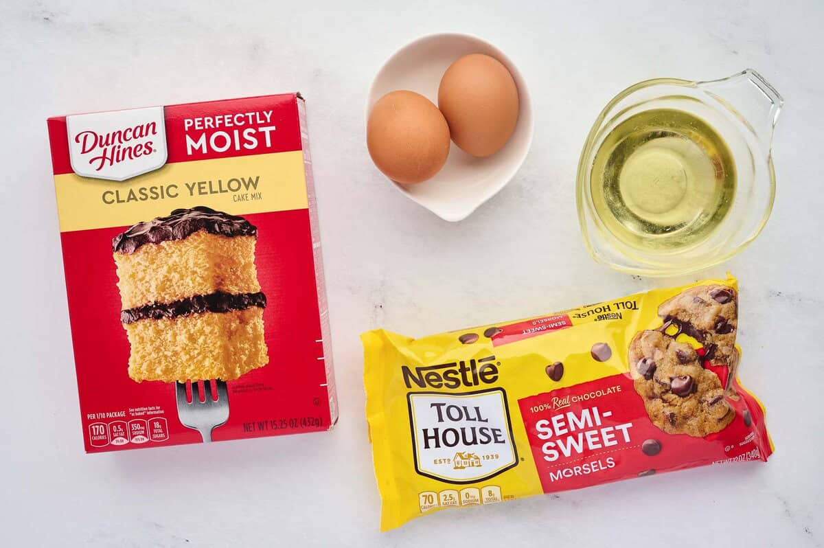 A box of cake mix, eggs, butter, and chocolate chips arranged on a clean kitchen counter in bright natural light