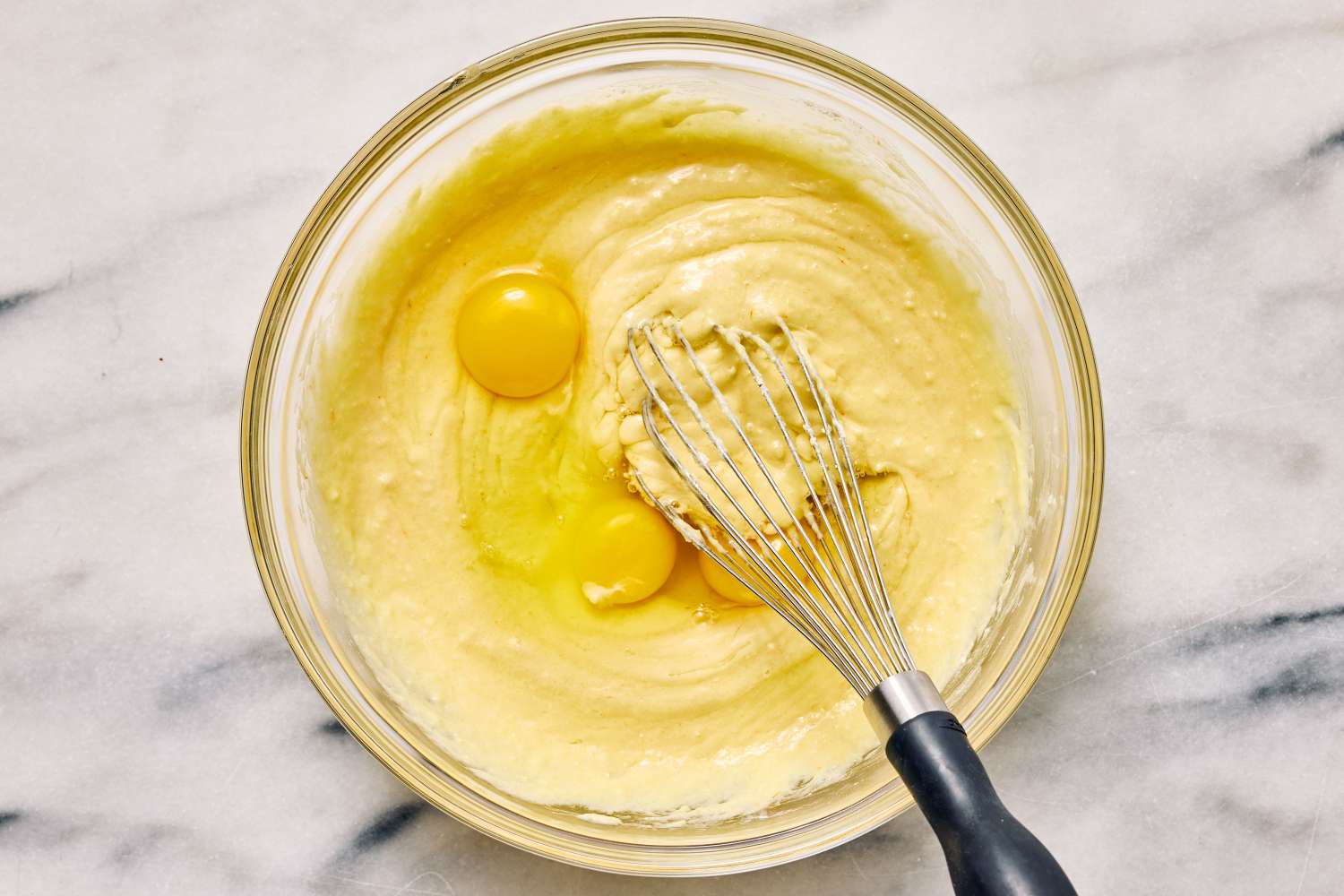 A box of yellow cake mix next to a bowl of melted butter and a whisk on a bright kitchen counter