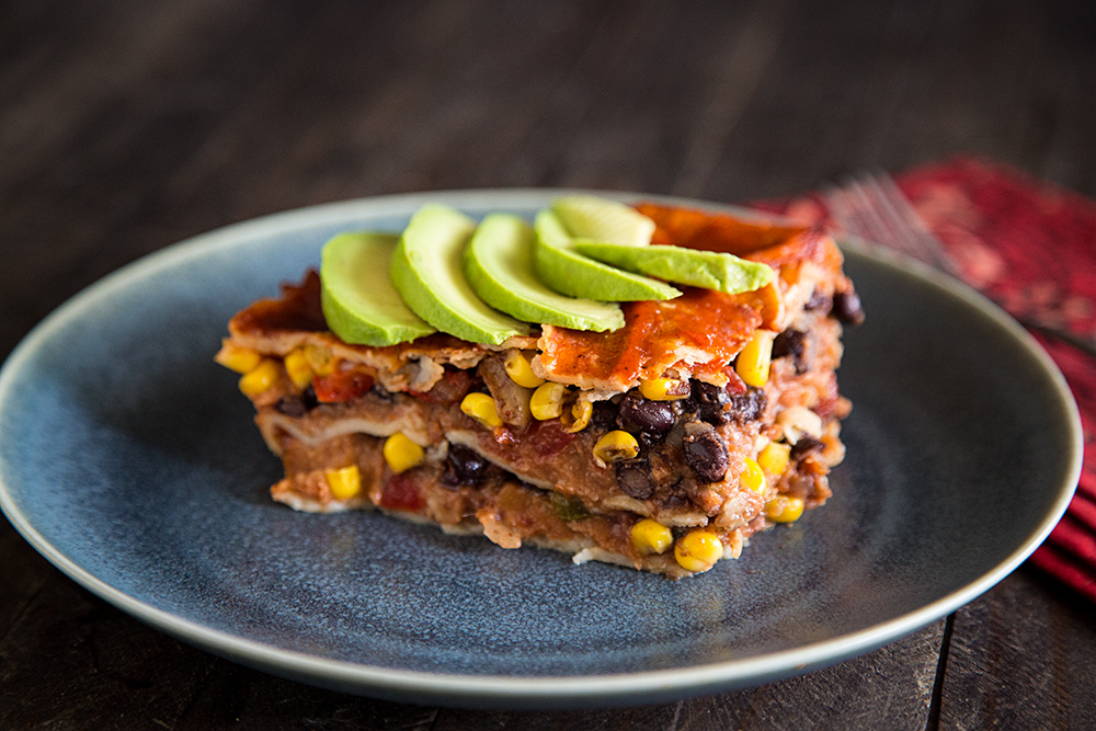 A bubbling Mexican casserole in a glass baking dish with browned, melty cheese on top, sitting on a neutral kitchen counter with warm natural light