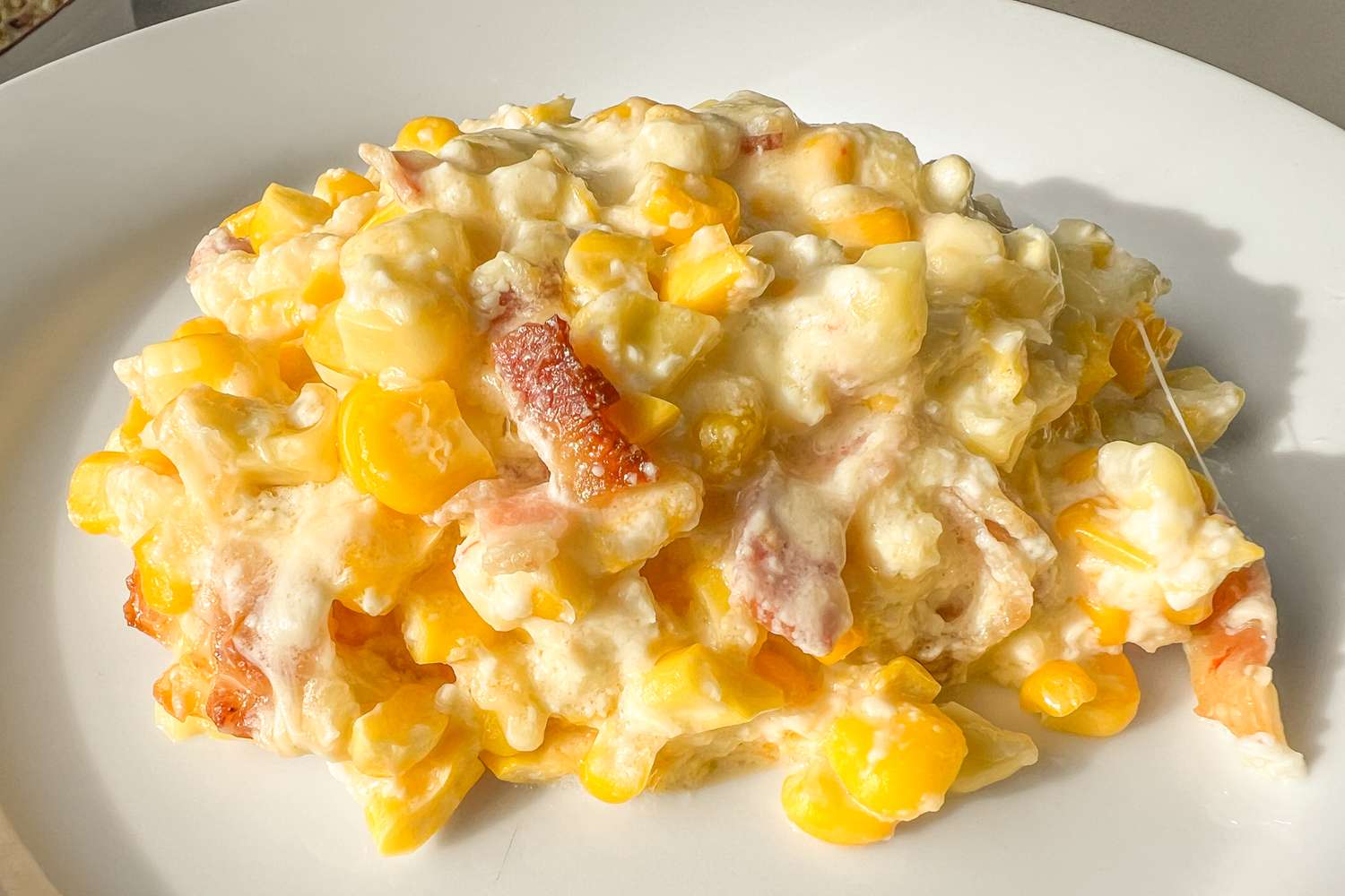 A bubbling cheesy baked corn casserole in a white ceramic baking dish with a golden top on a warm kitchen counter
