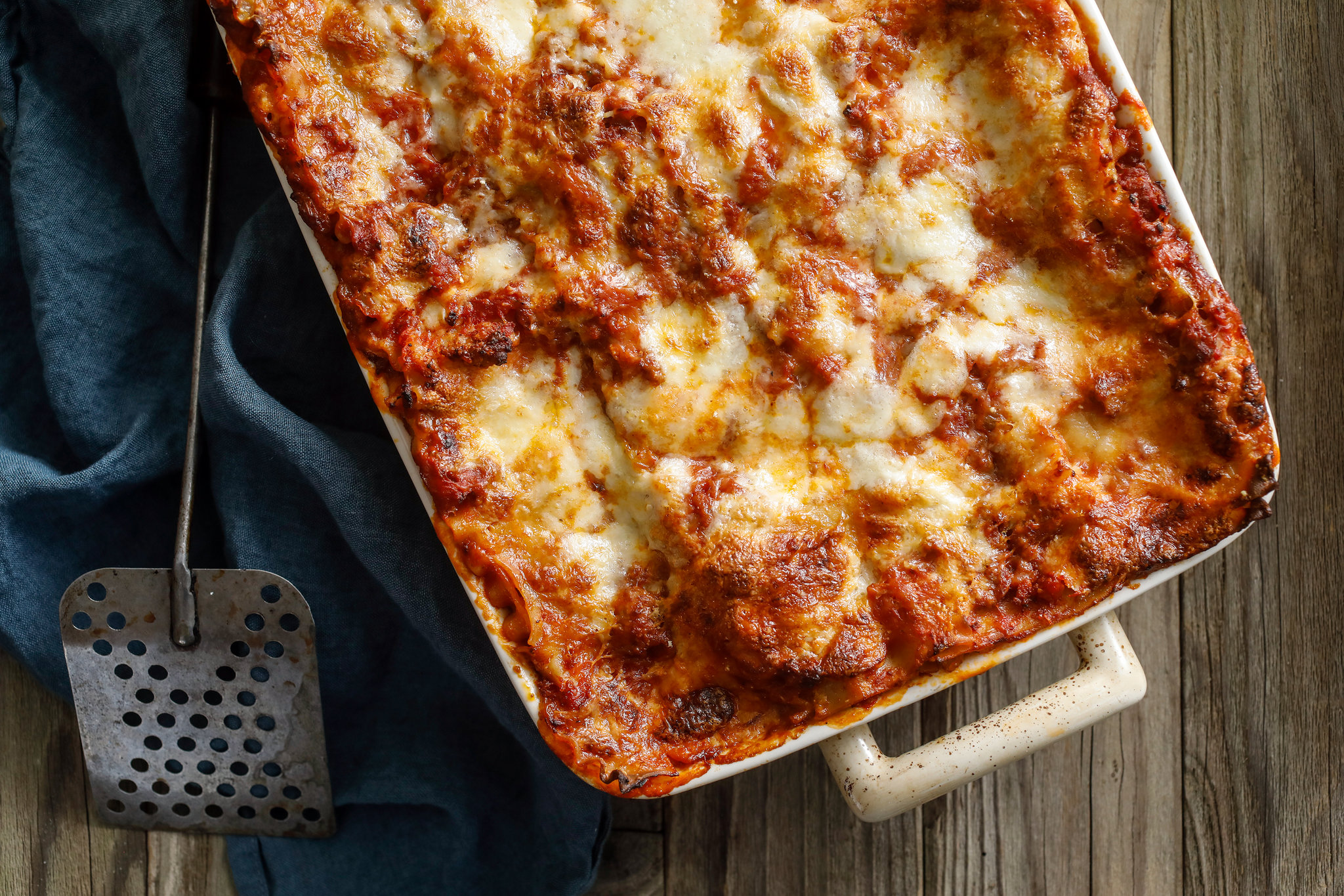 A bubbling classic Italian lasagna in a ceramic baking dish with a golden, melted mozzarella top resting on a wooden counter in a warm home kitchen
