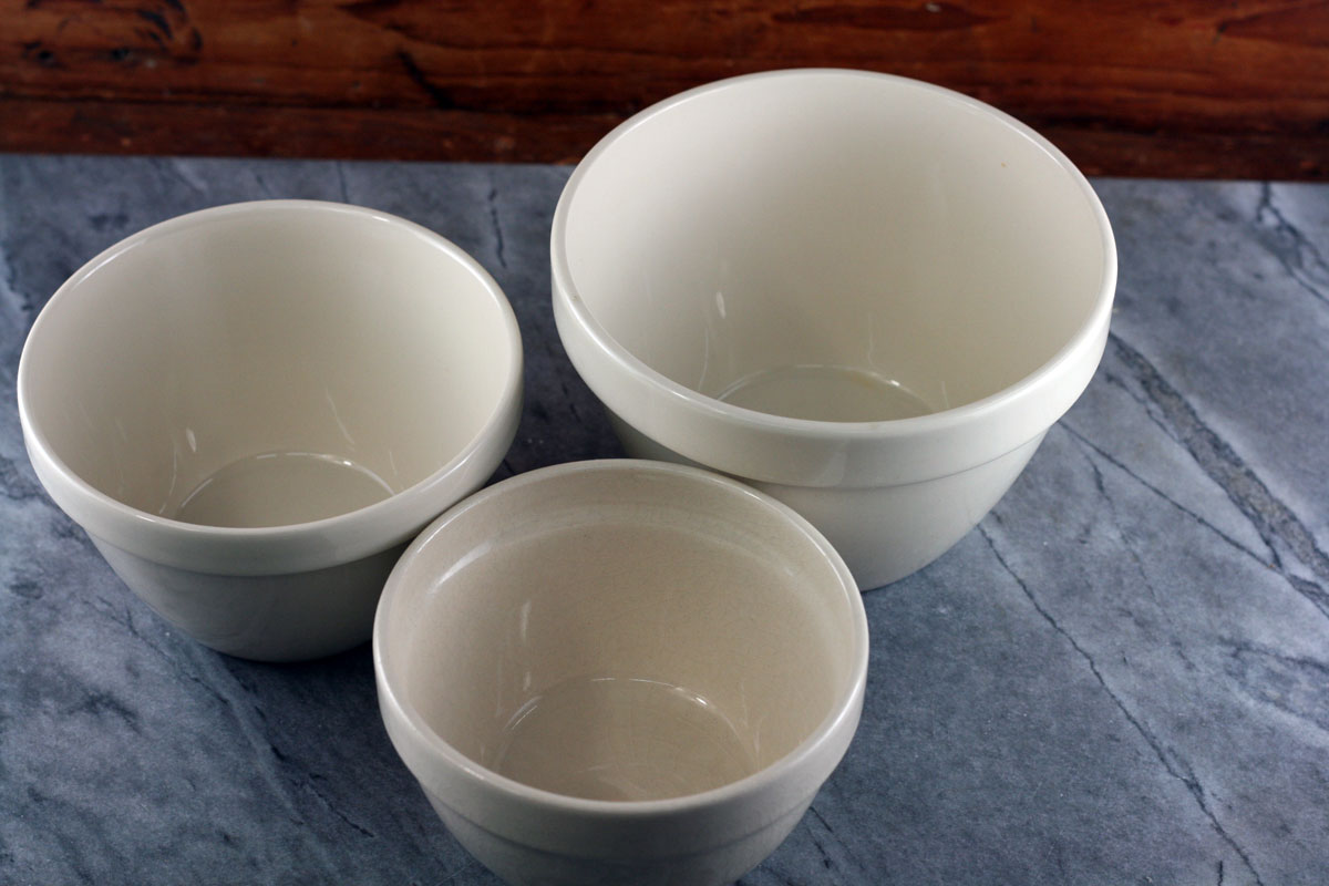 A butter-greased heatproof pudding basin on a kitchen counter next to a roll of parchment paper