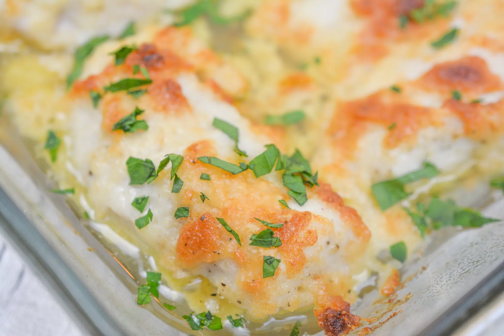 A casserole dish of baked chicken breasts topped with a golden, creamy Parmesan crust on a neutral kitchen counter with soft natural light