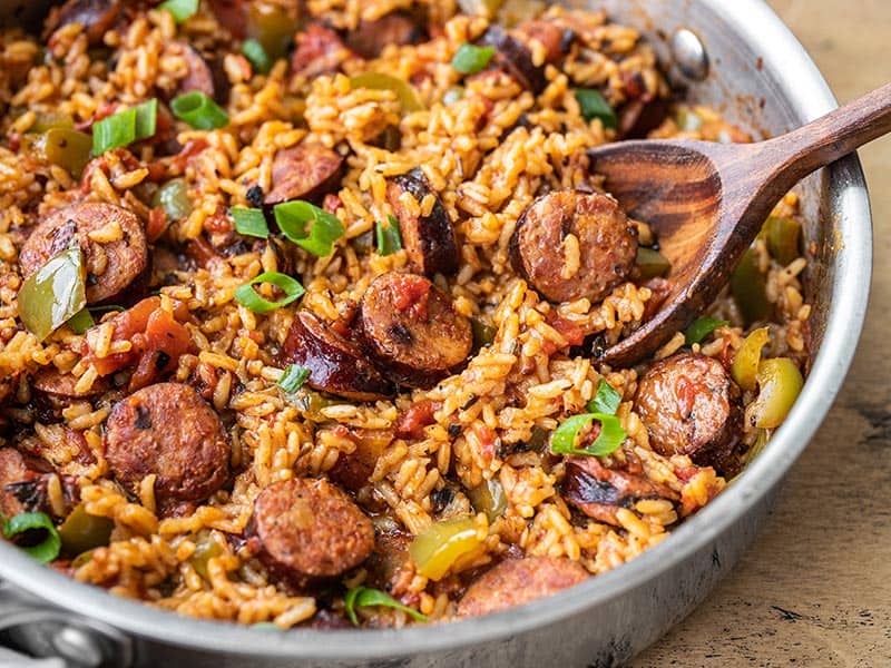 A cast iron pan filled with sausage and rice, with browned sausage slices, tender rice, and sautéed peppers, set on a warm kitchen counter with soft natural light