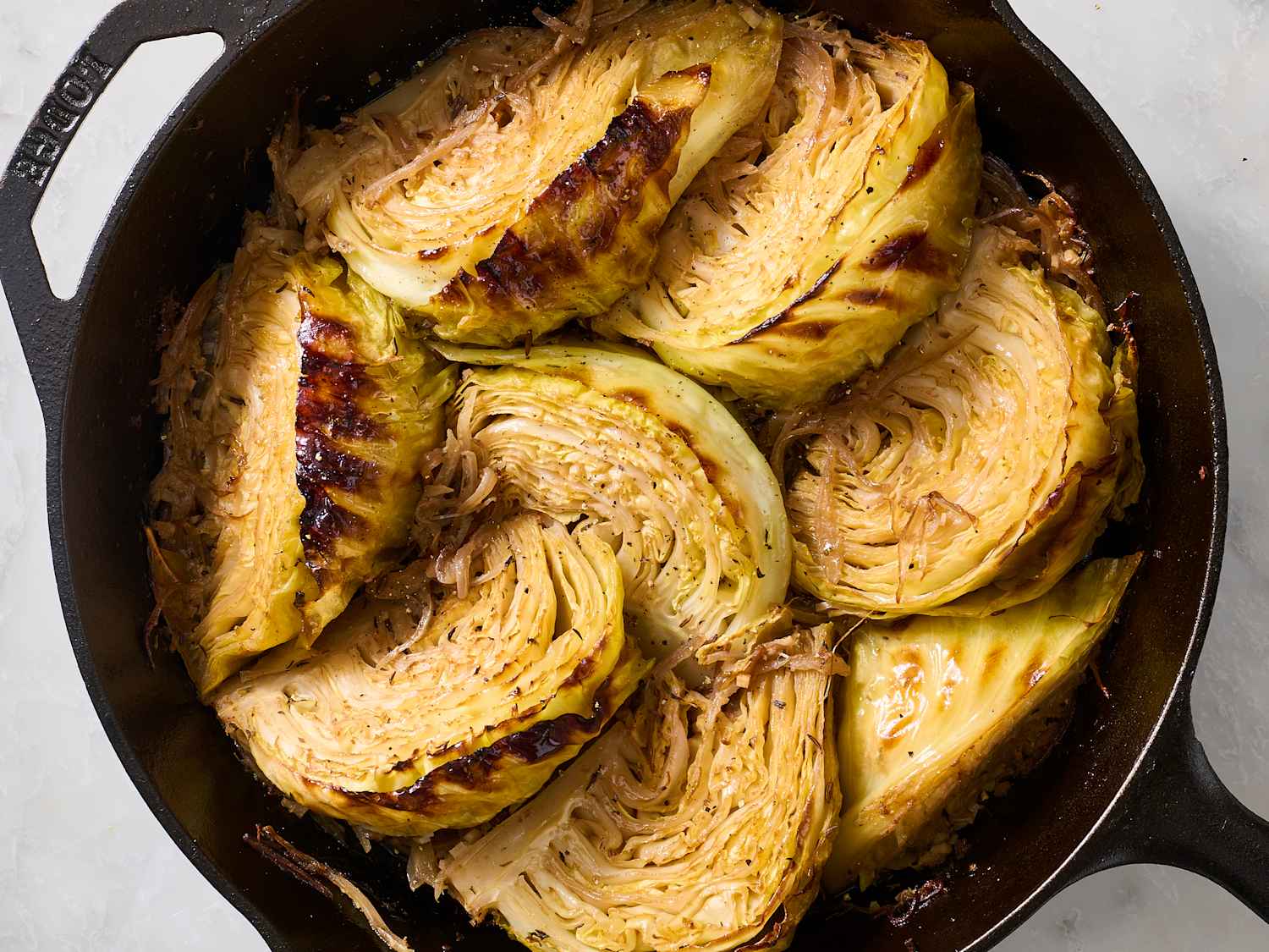 A cast iron skillet filled with buttery melted cabbage, browned edges visible, with a wooden spoon resting on the rim on a warm kitchen stove