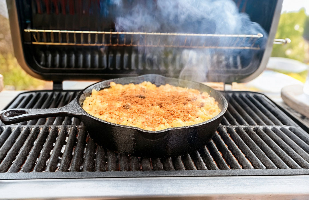 A cast iron skillet filled with creamy smoked mac and cheese with a golden toasted breadcrumb topping on a wooden table, warm natural kitchen lighting