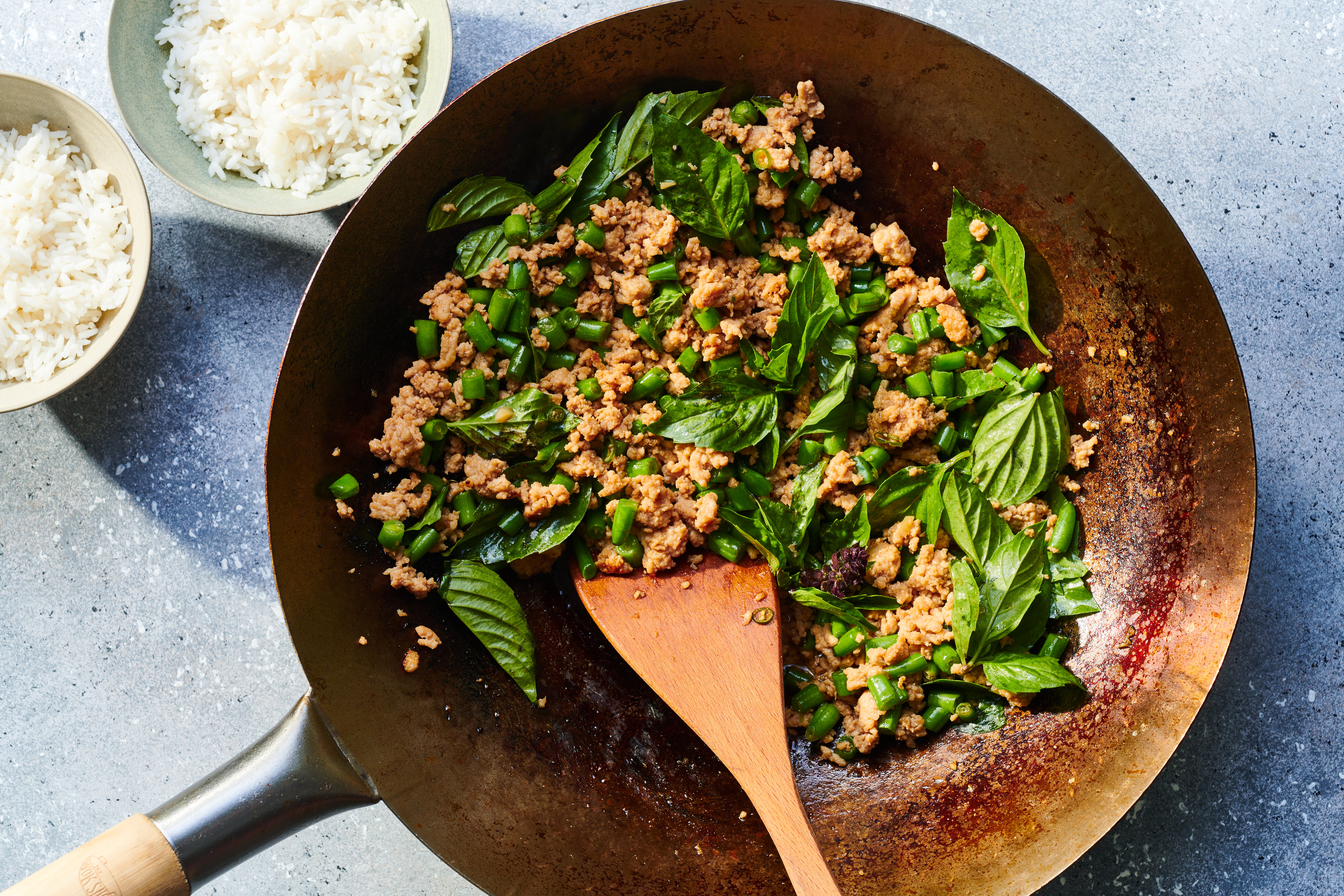 A cast iron skillet filled with glossy Asian basil chicken, with browned chicken pieces in a dark soy-garlic sauce and fresh basil leaves wilted on top, sitting on a warm lit kitchen stove