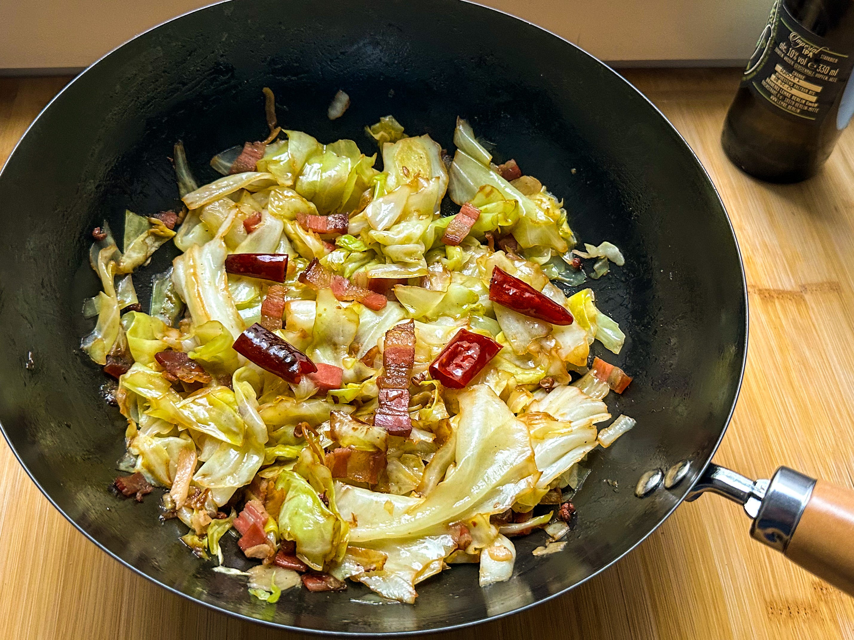 A cast iron skillet filled with glossy Asian cabbage stir-fry with crisp browned edges, sesame seeds, and sliced green onions on a warm kitchen counter