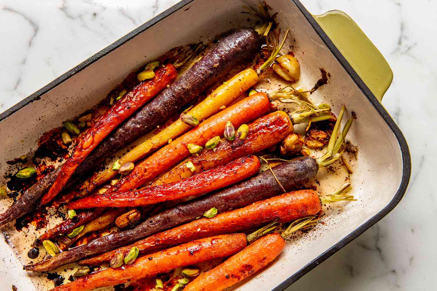 A cast iron skillet filled with glossy honey glazed carrots sprinkled with flaky salt and chopped parsley on a warm kitchen counter
