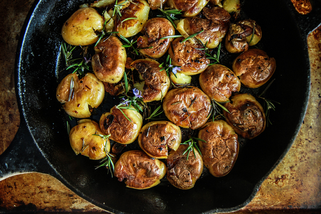 A cast iron skillet filled with golden crispy potatoes with browned edges, flecked with herbs and black pepper on a warm kitchen counter