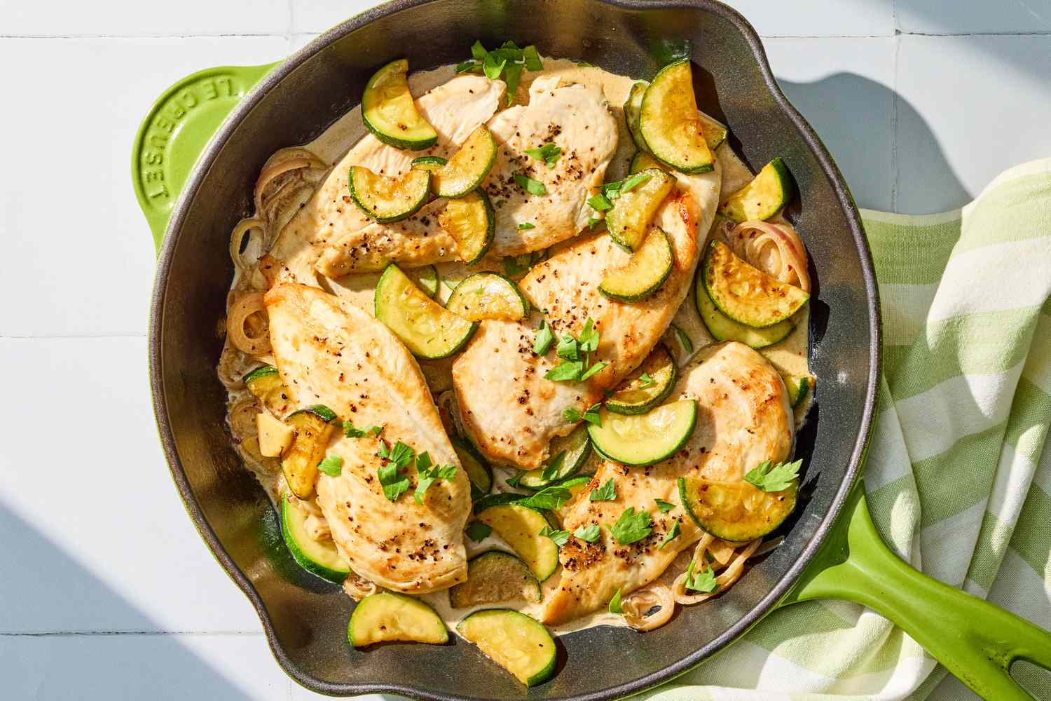 A cast iron skillet filled with golden seared chicken and sautéed zucchini coins in a creamy lemon Parmesan sauce, steam rising on a warm kitchen stove
