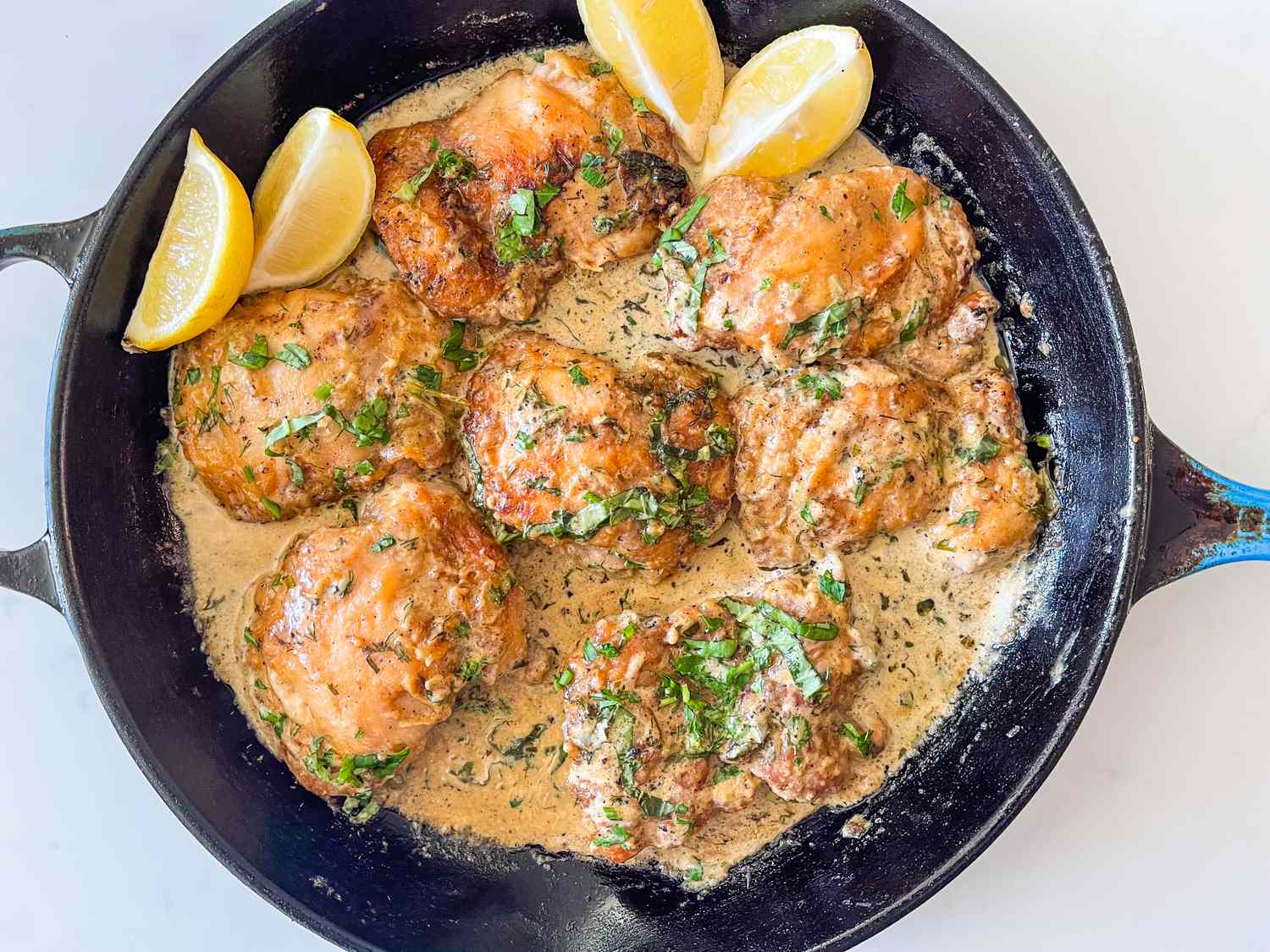 A cast iron skillet filled with golden seared chicken breasts simmering in a creamy lemon herb sauce, with fresh parsley scattered on top on a warm kitchen stove