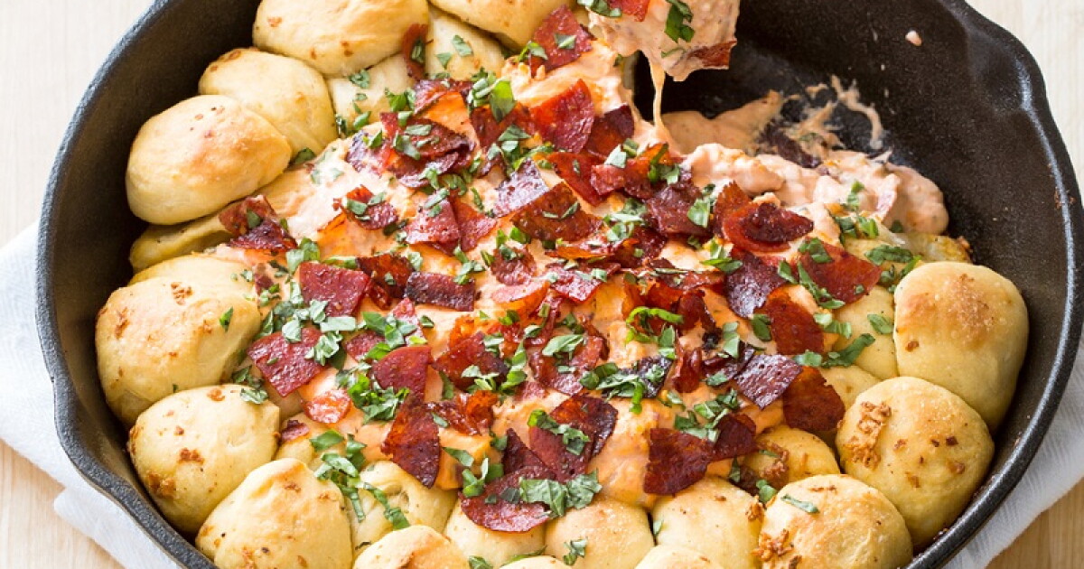 A cast iron skillet filled with hot pizza dip, bubbling marinara and melted mozzarella on top with curled pepperoni and a sprinkle of herbs, on a cozy kitchen counter with warm lighting