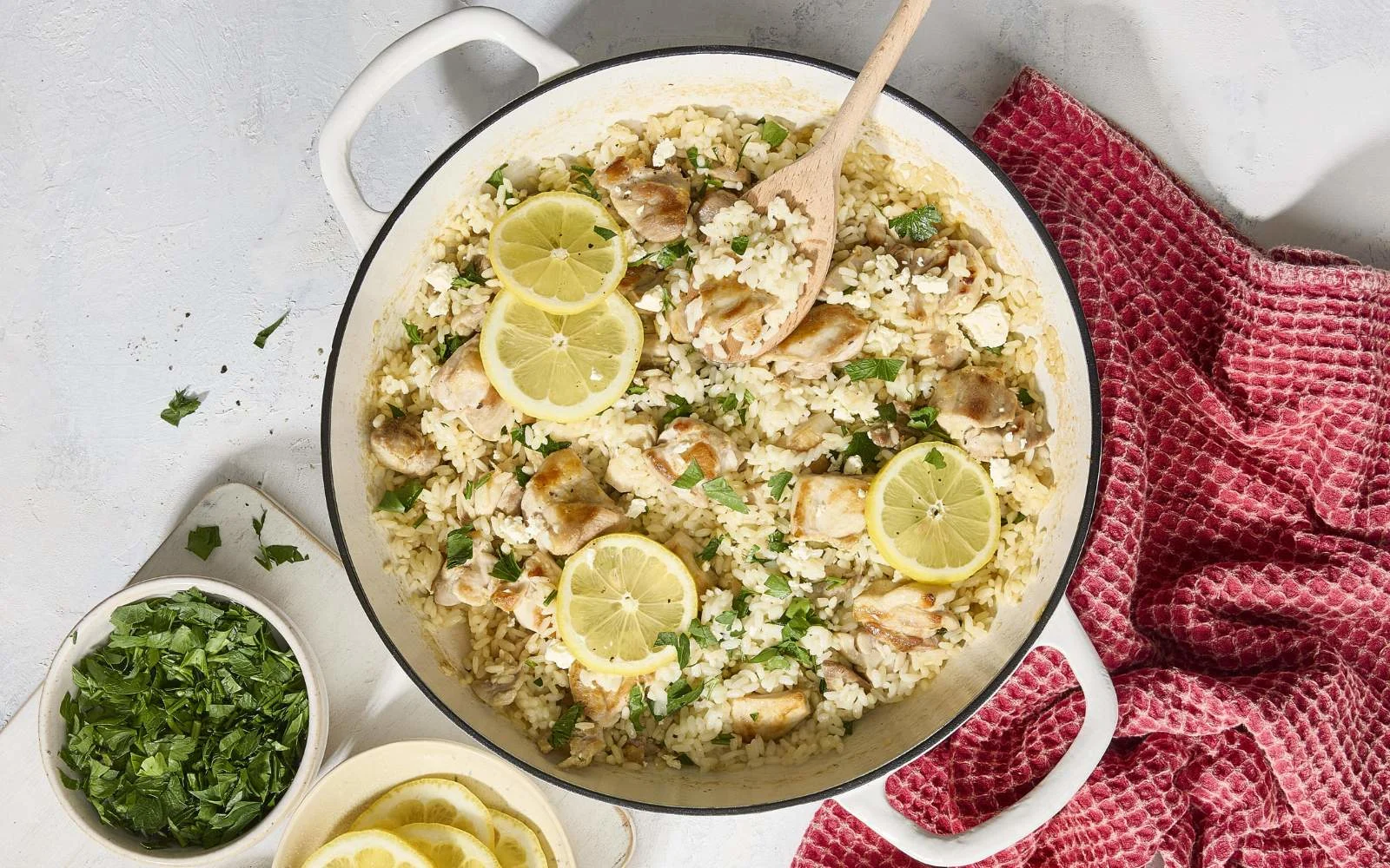 A cast iron skillet filled with lemon garlic chicken thighs nestled into fluffy rice with parsley and lemon slices on top, warm kitchen lighting
